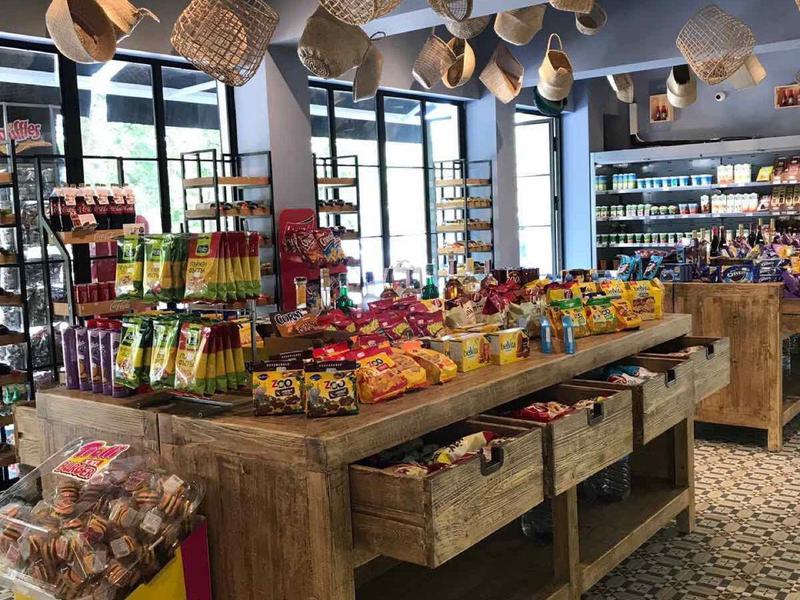 Ein heller Laden mit Holzregalen, bunten Snacks und hängenden Strohhüten an der Decke.