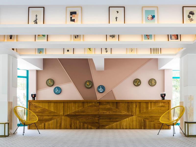 Moderner Empfangsbereich mit hölzerner Theke, gelben Stühlen, geometrischer Wandgestaltung und Kunstwerken.