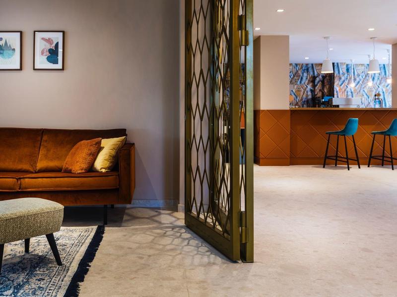 Moderner Raum mit braunem Sofa, Teppich, Trennwand und blau gepolsterten Barhockern.