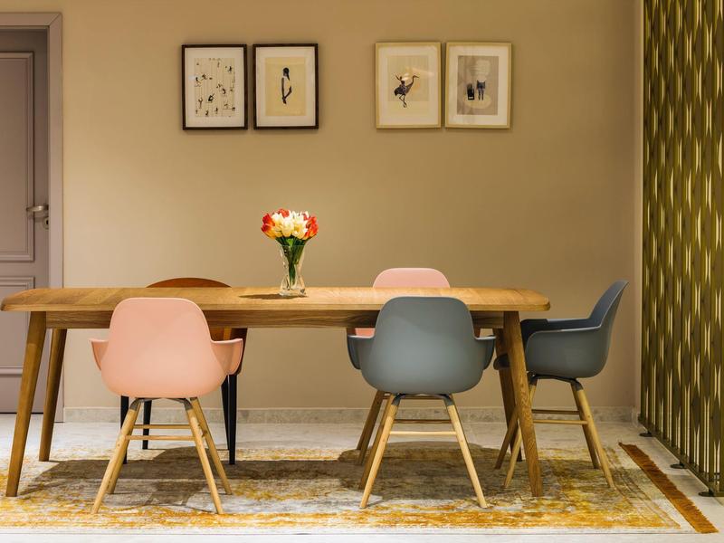 Esszimmer mit Holztisch, vier bunten Stühlen und Blumenstrauß in Vase auf Teppich.