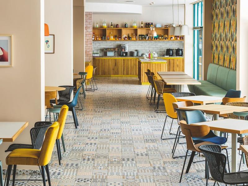 Modernes Café mit gelben und schwarzen Stühlen, Holztischen und beiger Fliesenboden im Tageslicht.