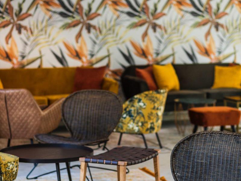 Moderner Wohnraum mit gemusterten Tapeten, Korbstühlen, bunten Sofas und hängenden Lampen.