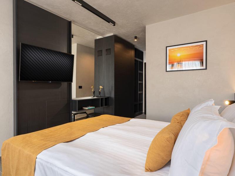 Modernes Hotelzimmer mit großem Bett, gelben Akzenten, Flachbildschirm und gerahmtem Bild an der Wand.