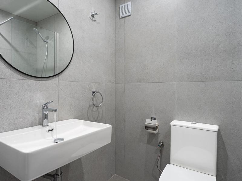 Minimalistisches Badezimmer mit grauen Fliesen, rechteckigem Waschbecken und rundem Spiegel.