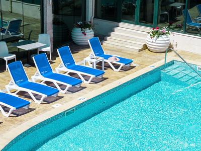 Blauw zwembad naast terras met blauwe ligstoelen en witte bloempotten.