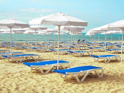 Veel blauwe ligbedden met witte parasols op een zandstrand met uitzicht op zee.