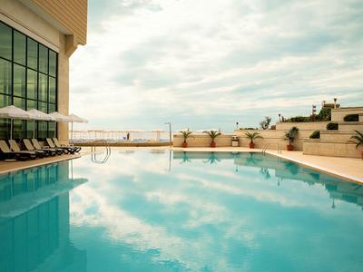 Modern buitenzwembad met ligstoelen en glazen ramen, rustige lucht weerspiegeld in het water.