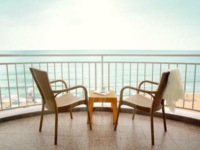 Twee stoelen met een klein tafeltje ertussen op een balkon met uitzicht op zee.