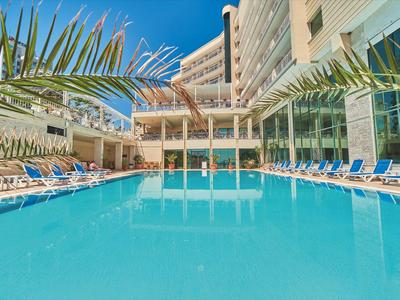 Piscina moderna de hotel rodeada de tumbonas y palmeras bajo un cielo azul claro