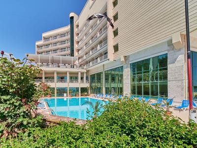 Hotel con piscina al aire libre, tumbonas y jardín bajo un cielo azul claro
