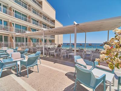 Terraza exterior de un hotel con mesas, sillas y vista al mar bajo un cielo despejado.
