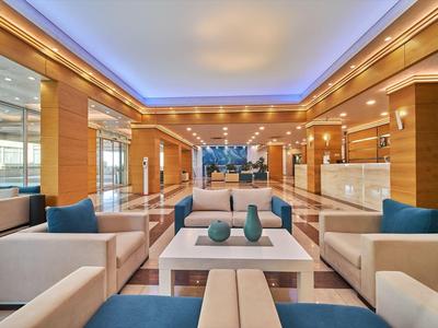 Moderne hotel lobby met comfortabele banken, witte tafels en blauwe accenten bij warm licht.