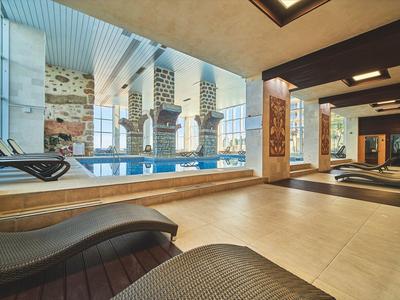 Modern binnenzwembad met hoge ramen, ligstoelen en stijlvolle inrichting.