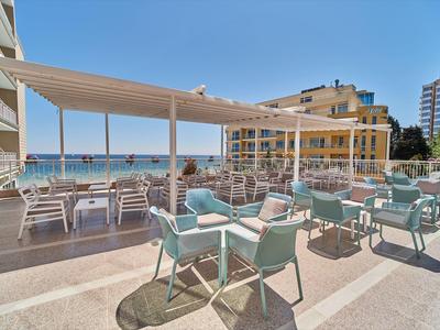Buitenterras van een hotel met tafels en stoelen met uitzicht op zee bij zonnig weer.