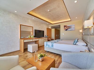 Modern hotelkamer met tweepersoonsbed, bank, tv en houten meubels.