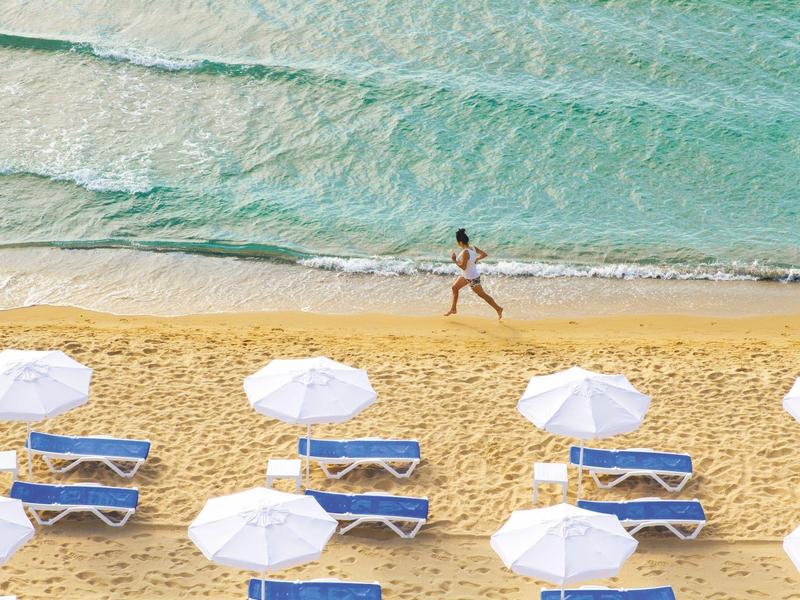 Een rustig strand met witte parasols en ligbedden, een persoon rent langs de kust.
