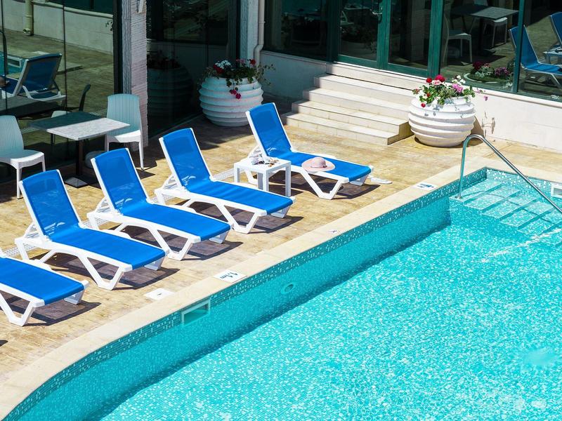 Blauw zwembad naast terras met blauwe ligstoelen en witte bloempotten.