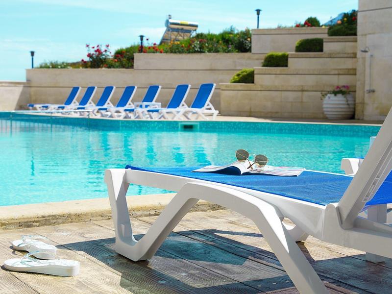 Zwembadgebied met ligstoelen en twee mensen in het water, lichte stenen muren op de achtergrond.