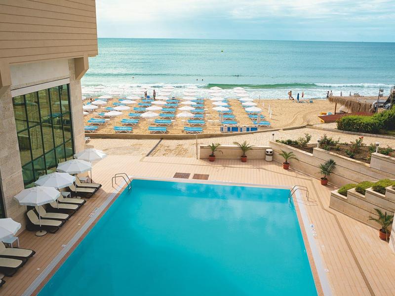 Hotelzwembad met ligstoelen en parasols op het strand naast de zee bij helder weer.
