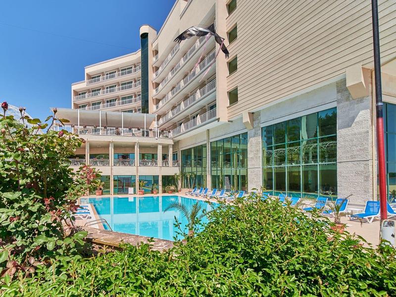 Moderne hotelzwembad met ligstoelen en groene struiken op de voorgrond.