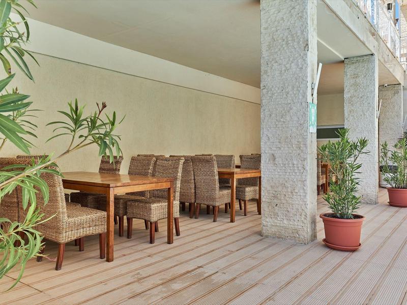 Overdekt buitengedeelte met houten vloer, tafels, stoelen en potplanten naast zuilen.