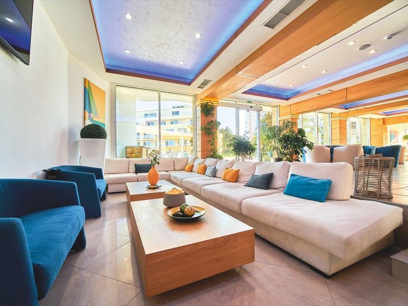 Lichte hotelkamer met moderne inrichting, banken en houten plafond met blauwe accentverlichting.