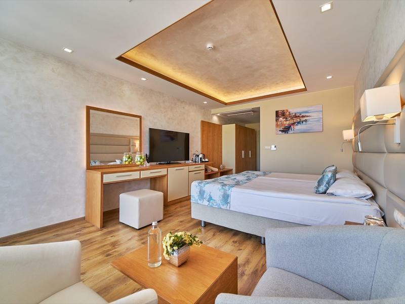 Modern hotelkamer met tweepersoonsbed, bank, tv en houten meubels.