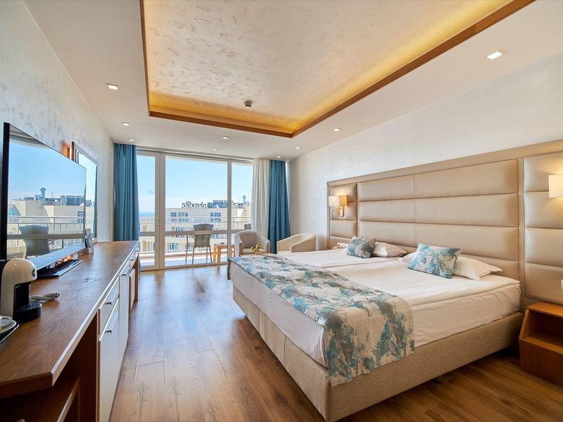 Lichte hotelkamer met tweepersoonsbed, houten vloer en balkon met uitzicht op de stad