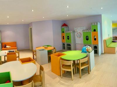 Sala giochi per bambini luminosa con tavoli colorati, sedie e armadietti per giocattoli.