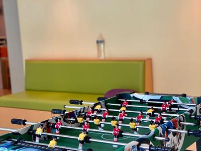 Stół do piłkarzyków z kolorowymi zawodnikami w nowoczesnym pokoju z zieloną częścią wypoczynkową.