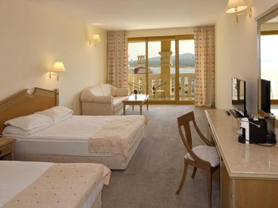 Camera d'hotel luminosa con tre letti, poltrona, scrivania e balcone con vista sulle montagne.