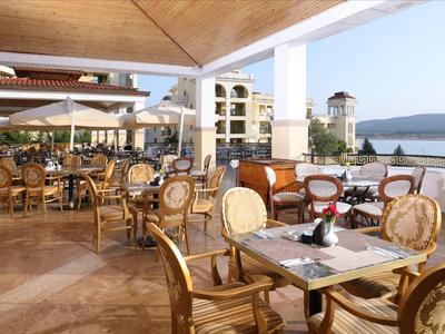 Ristorante all'aperto con mobili in legno e vista sul mare con tempo soleggiato.