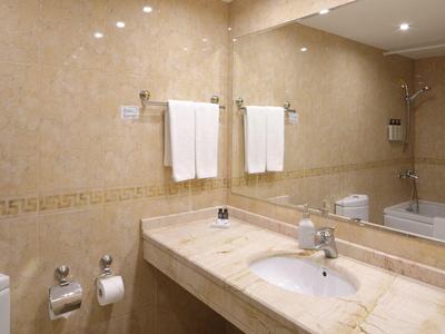 Bagno luminoso con marmo beige, grande specchio e vasca da bagno.