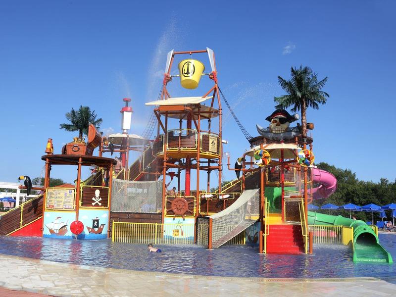 Struttura gioco colorata in parco acquatico con scivoli e palme sotto un cielo limpido.