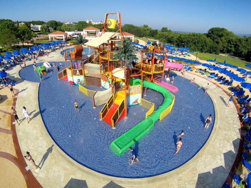 Grande parco acquatico con scivoli e piscine, circondato da lettini e verde.