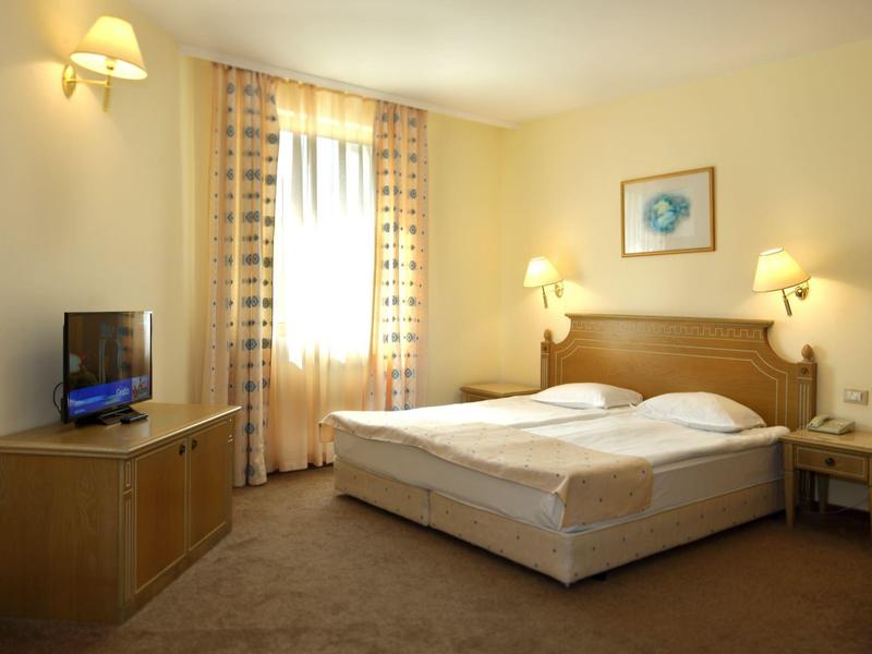 Camera d'hotel luminosa con letto matrimoniale, due lampade da comodino, TV e finestra con tende.