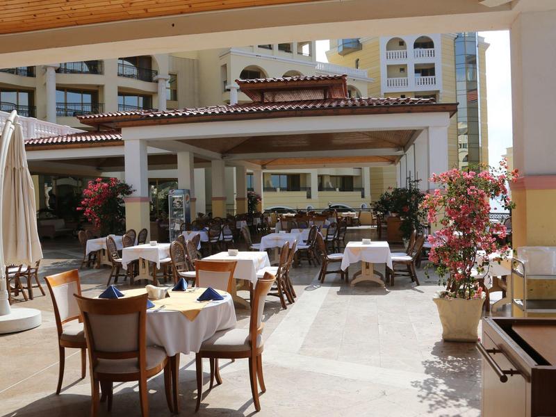 Area pranzo all'aperto con tavoli apparecchiati e sedie accanto a un edificio alberghiero.