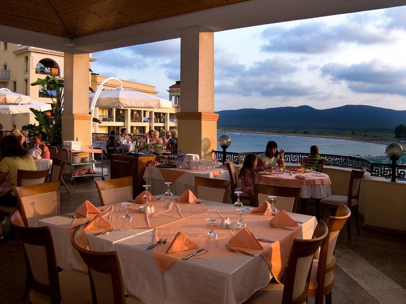 Ristorante all'aperto con tavoli apparecchiati e vista su lago e montagne al tramonto.