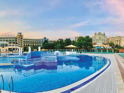 Ruim hotelresort met een groot zwembad en ligstoelen bij zonsondergang.