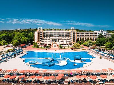 Groot resort met dolfijnvormig zwembad, omgeven door ligstoelen en bomen.