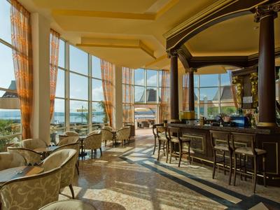 Lichte hotelbar met grote ramen, hoge plafonds en uitzicht op zee.