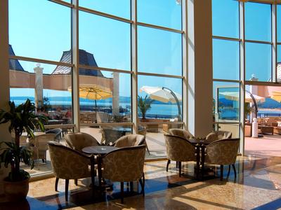 Lichte hotellounge met grote ramen en uitzicht op zee, zithoeken van rotan.