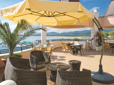 Terras met rieten meubels, gele parasol en uitzicht op zee en bergen.