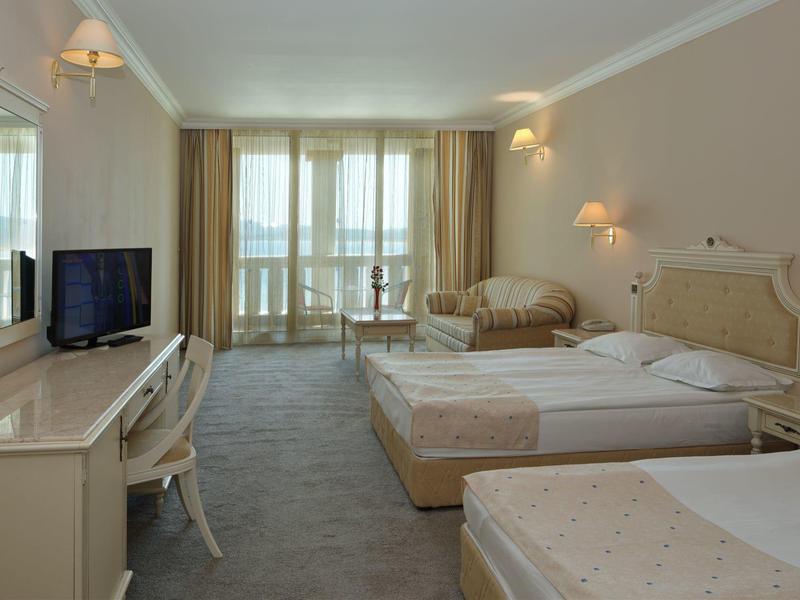 Lichte hotelkamer met twee bedden, fauteuils en flatscreen-tv voor grote ramen.