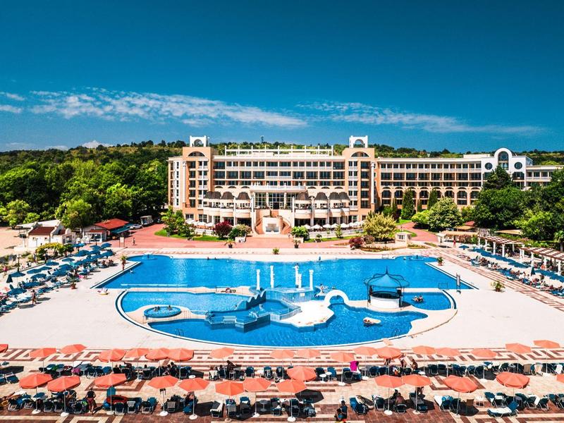 Groot resort met meerdere zwembaden, ligstoelen en veel groen onder een blauwe lucht