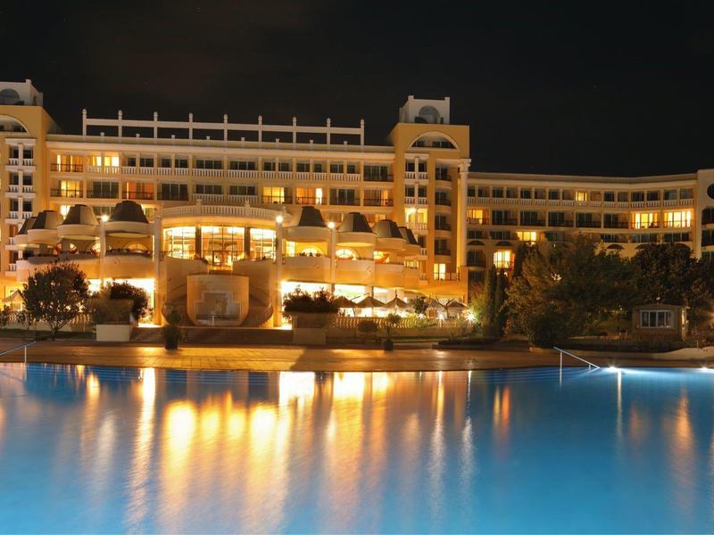 Verlicht luxe hotel 's nachts met groot reflecterend zwembad op de voorgrond.