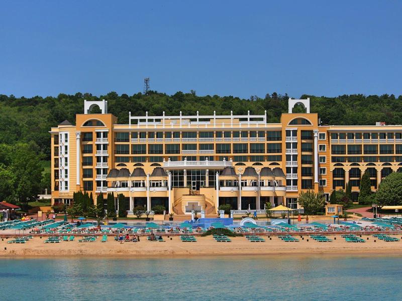 Groot hotel met terracottavak aan het strand met parasols en blauwe zee