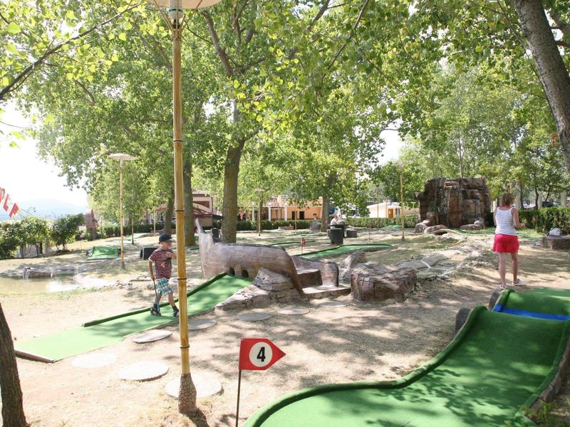 Buiten minigolfbaan met bomen en gasten die spelen op een zonnige dag.