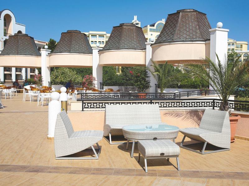 Open zithoek met moderne stoelen en tafels op een zonnig terras naast een hotelgebouw.