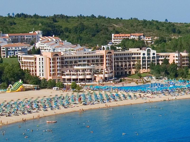Groot hotel met parasols op zandstrand voor beboste heuvel